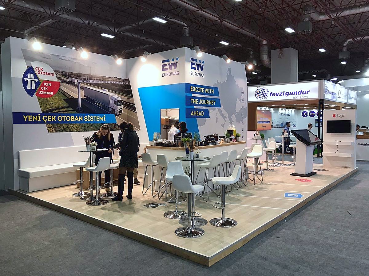 Eurowag exhibition stand at Logitrans 2019: Clean white surfaces, digital screens and bar-height meeting points support quick conversations along the open frontage