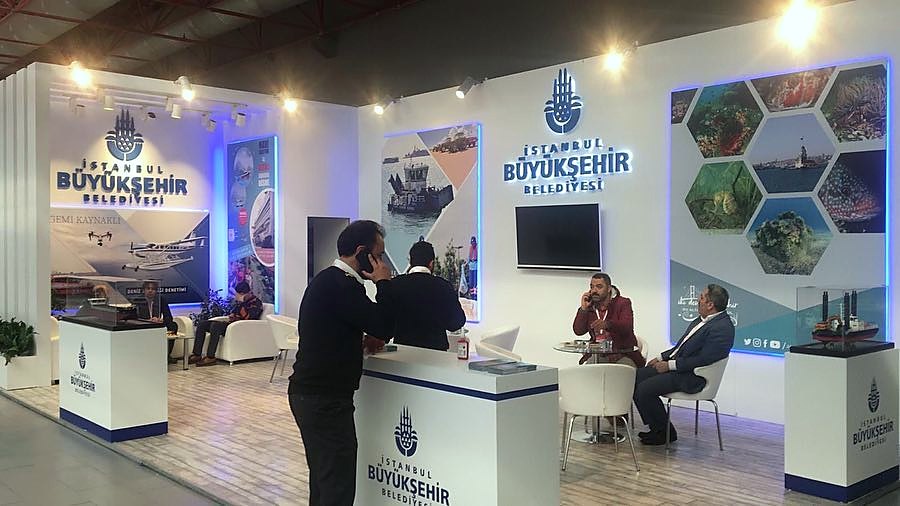 Stand d’exposition İstanbul Büyükşehir Belediyesi au salon CNR Eurasia Boat Show 2019 : De grands graphismes urbains et maritimes, une façade ouverte et un espace de réunion rendent la communication publique visible