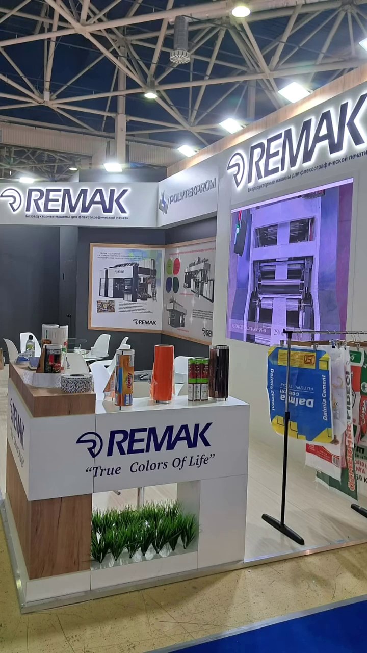 Stand d’exposition Remak au salon RUPLASTICA 2024 : Des surfaces sombres, des accents de bois et un écran intégré structurent clairement l’accueil et l’espace de réunion sur une surface compacte